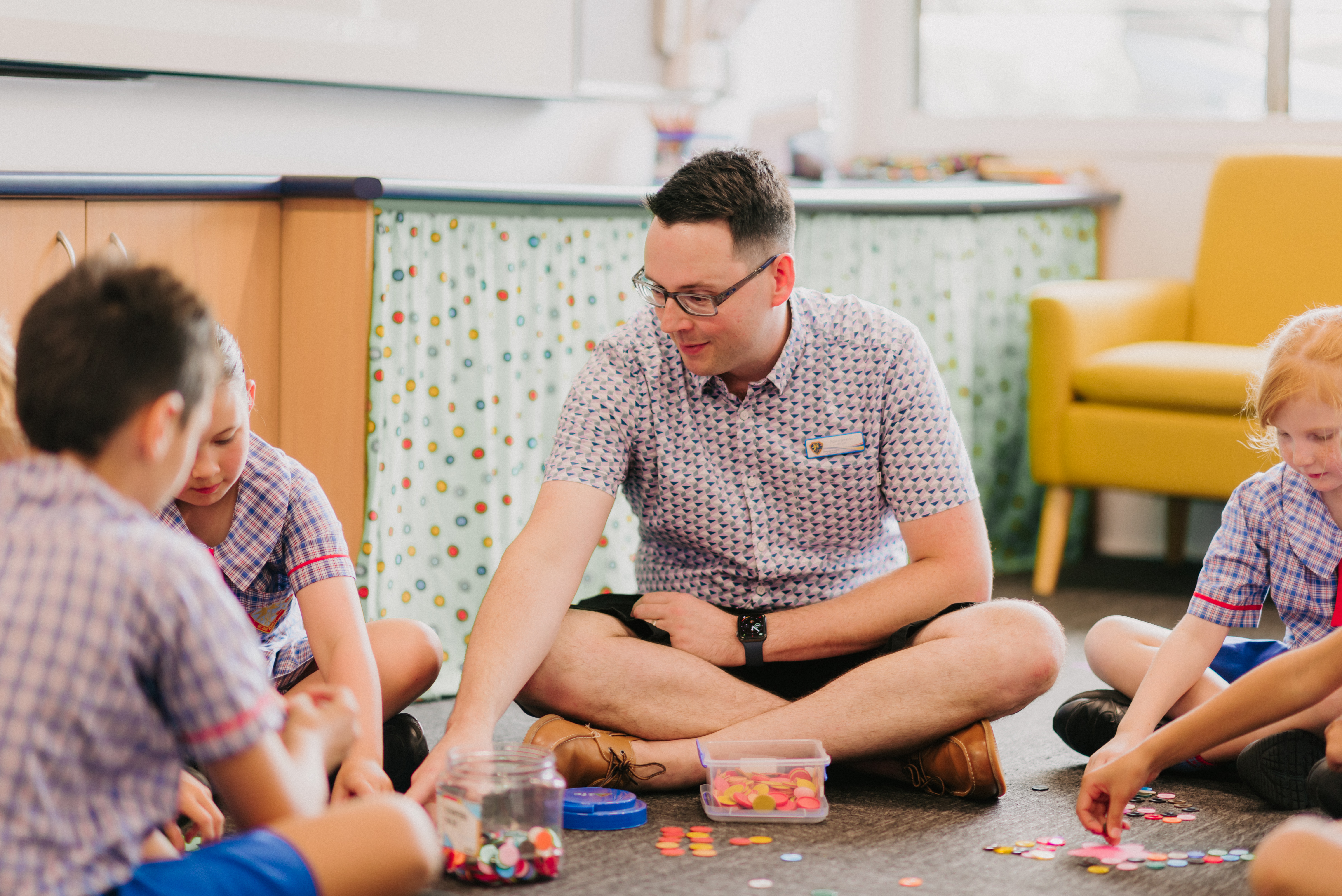 Adult and students sitting in a circle on a classroom floor using counters for a learning activity.