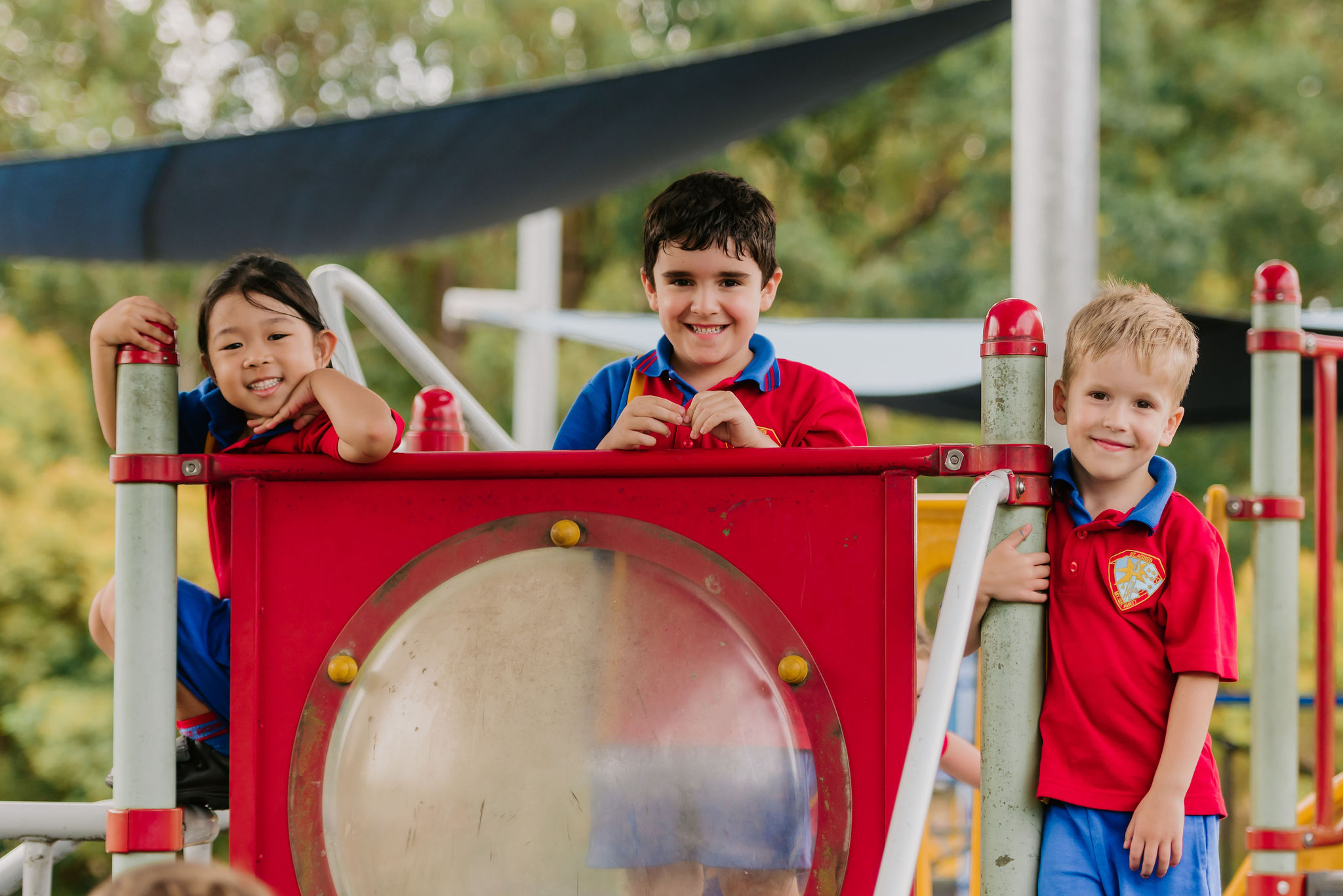 Three students in school uniform standing on outdoor playground equipment together.