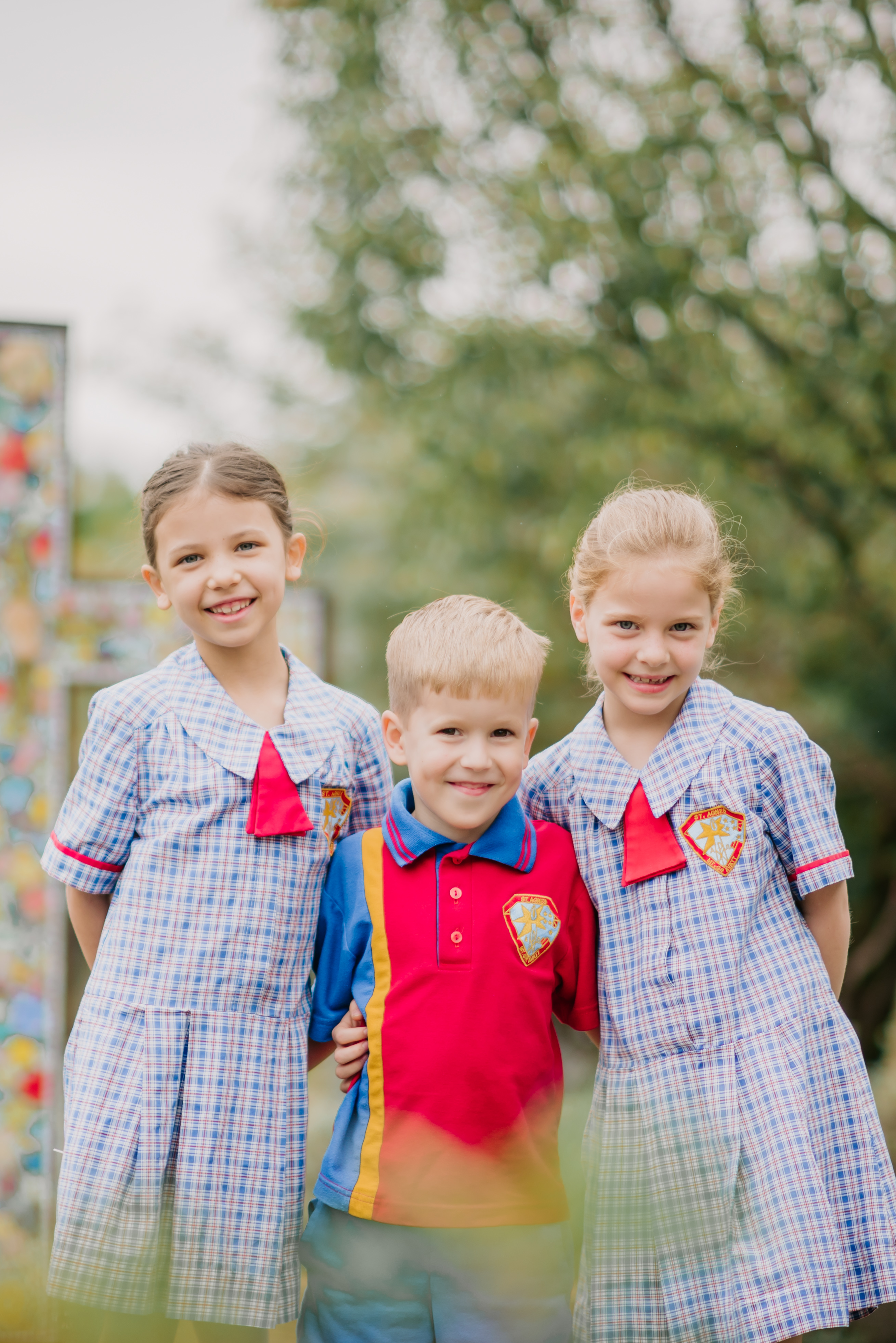 Three students in school uniform standing together outdoors in a garden setting.