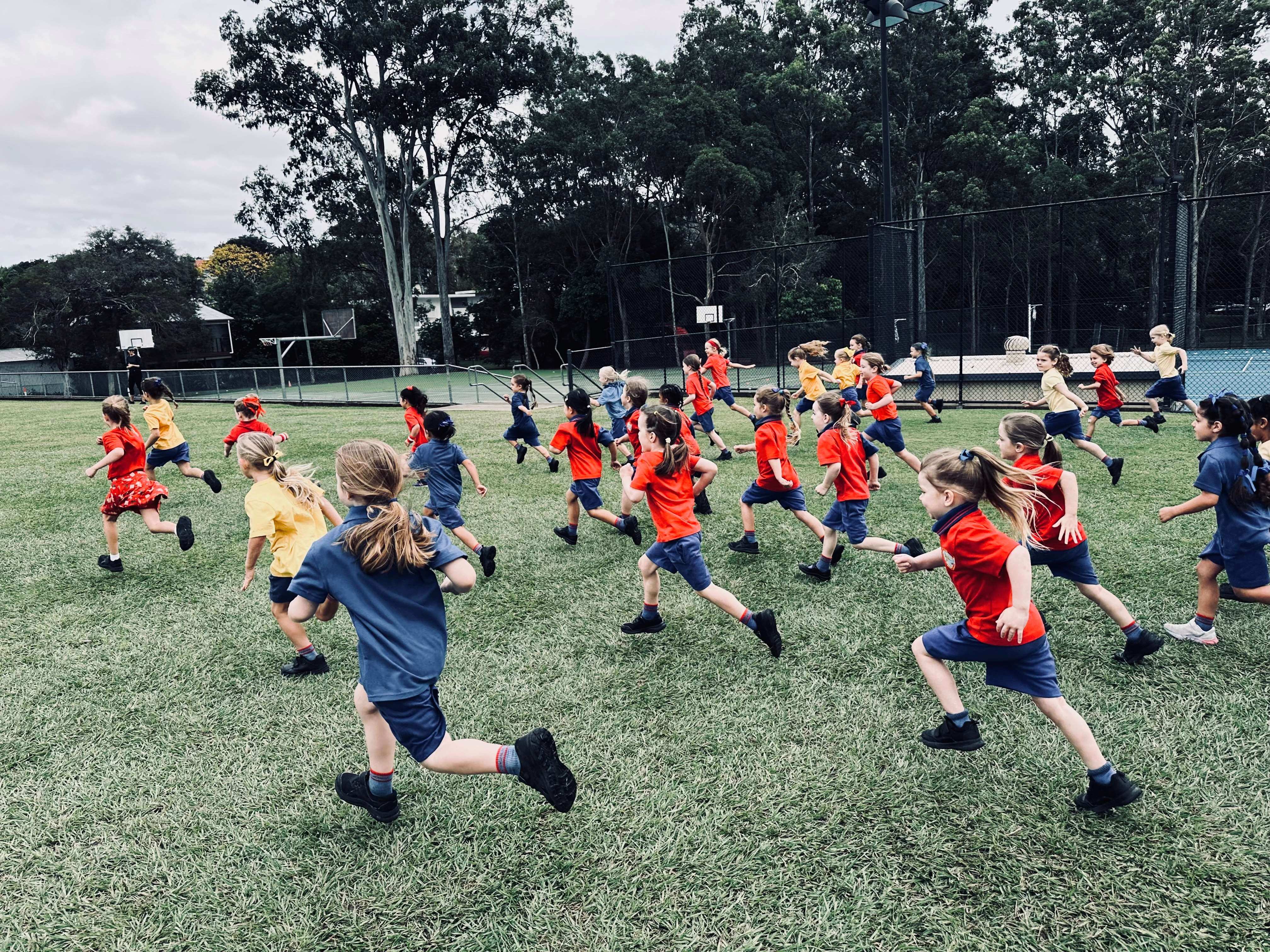 Students in school uniform running together across a grassy school field during an outdoor activity.