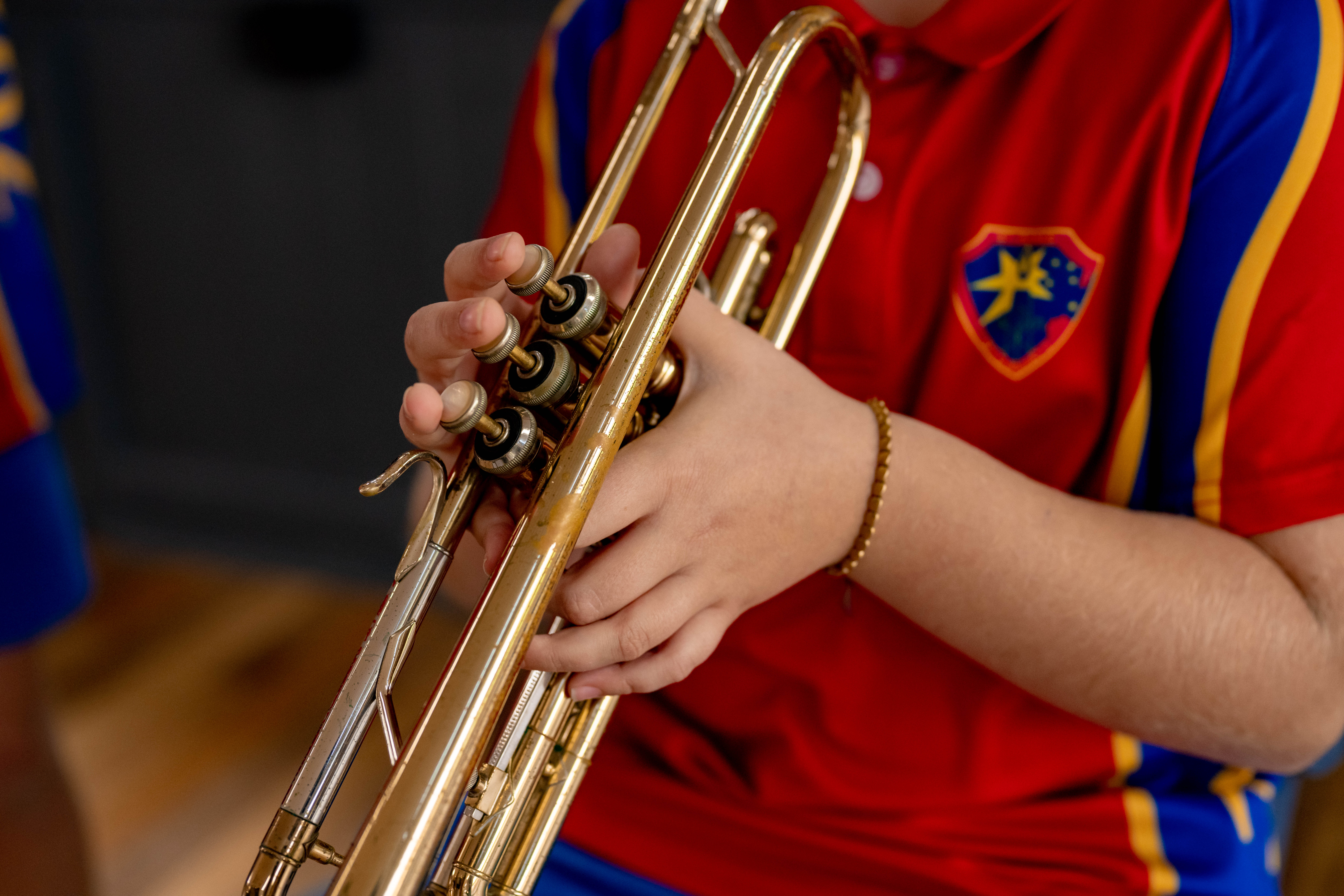 Close‑up of a student’s hands pressing the valves of a brass trumpet during a school music lesson.