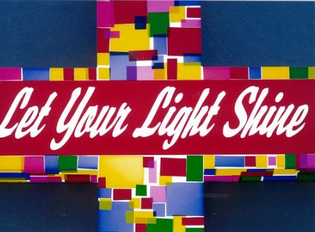 Bright mosaic‑style cross graphic with a red banner reading “Let Your Light Shine”.
