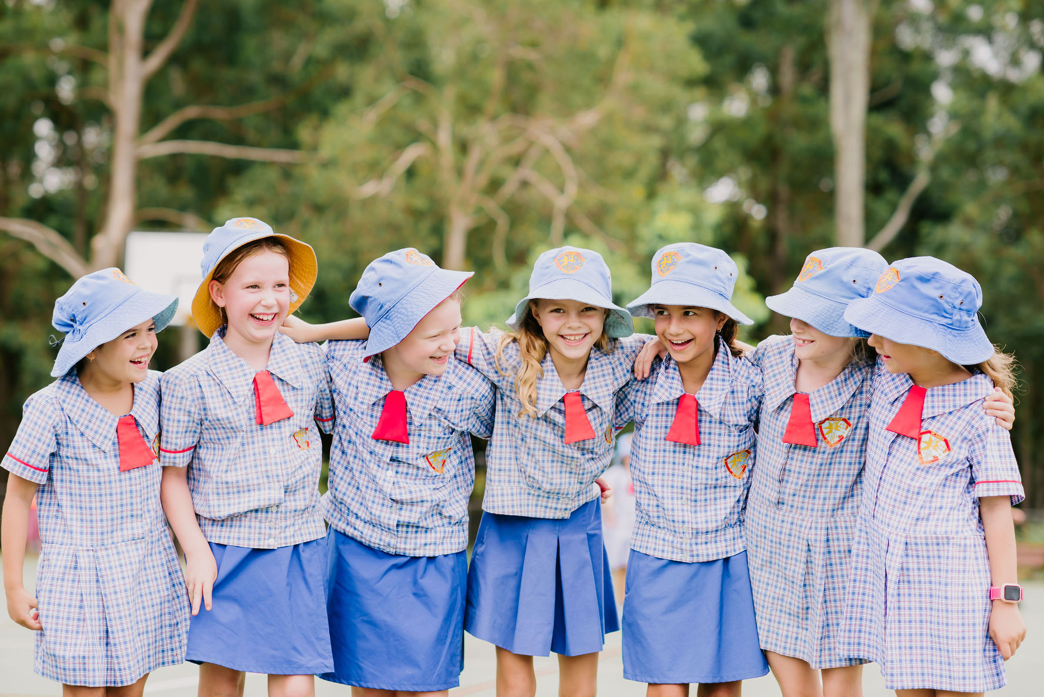 Group of students in school uniform standing side by side outdoors with arms around each other.