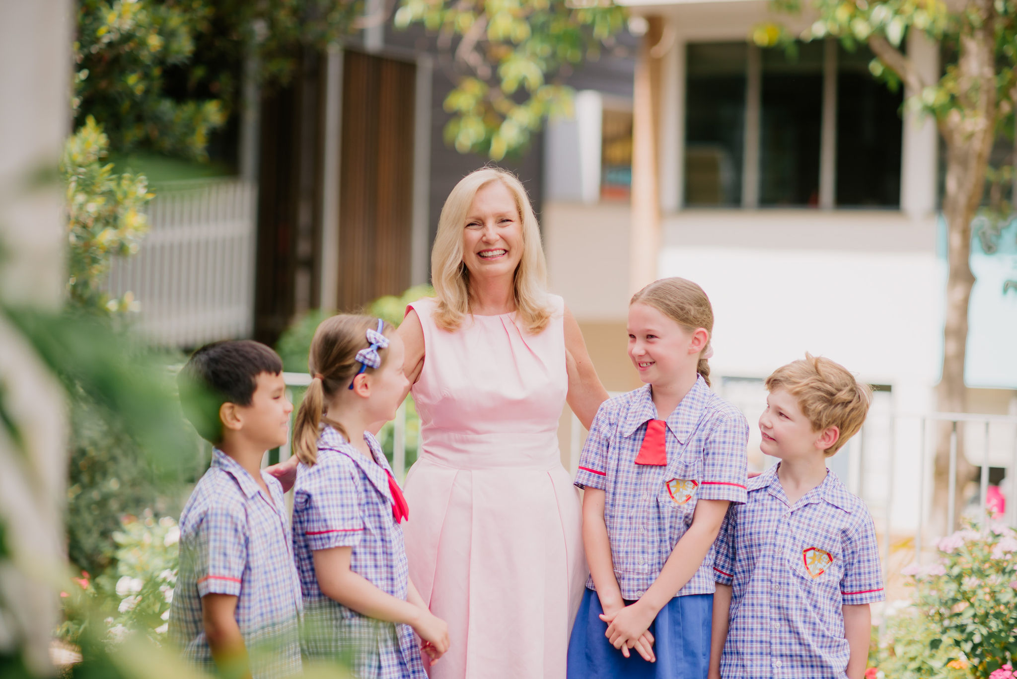 Adult standing outdoors with a small group of students in school uniform, talking together in a garden setting.
